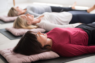Three women laying down on yoga mats in a Yoga of Stillness session