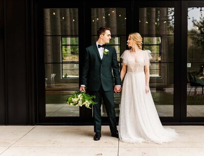 Bride and groom dancing in front of a wood and glass window building