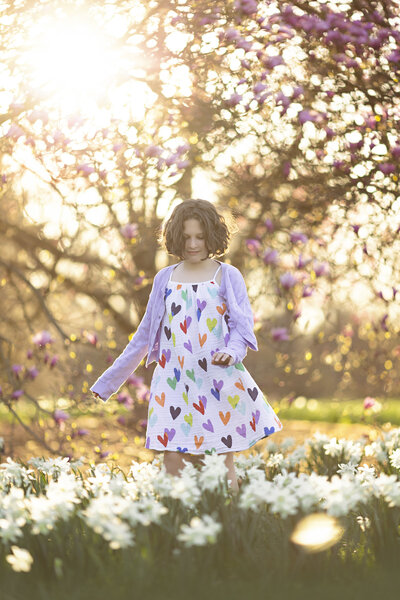 Young girl in rainbow hearts dress in a field of white flowers in Central NJ park.