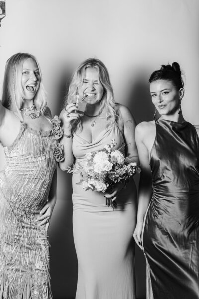Candid black and white portrait of three women laughing and celebrating with drinks and flowers at a Vogue Portrait photo booth in Richmond, VA.