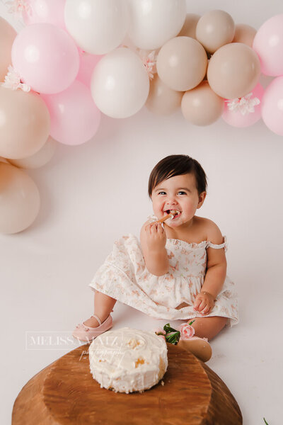 one year old smiling while smashing her one year cake in a shelby township mi photography studio