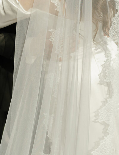close detail of a groom's hands holding his bride in sunlight, through her ethereal lace cathedral veil