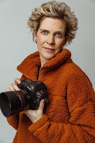 Photographer Sarah Monson holding a camera and wearing an orange fleece