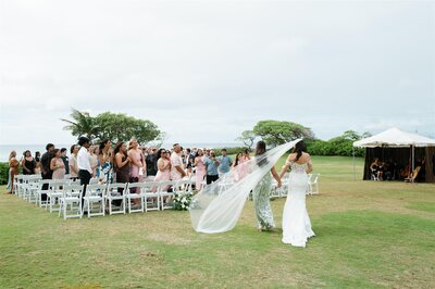 A person holding hands with a person in a wedding dress as they walk down the aisle 
