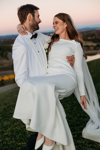 Bride carried by her groom during sunset photos at the National Arboretum Canberra. Photo by Acacia & Grace Wedding Photography