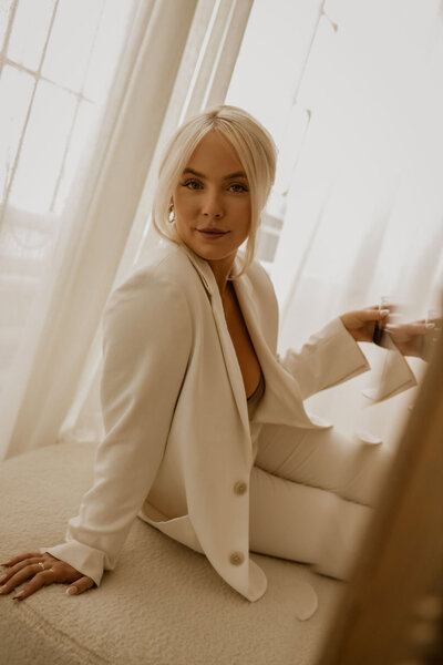 7 figure sales expert natasha zoryk dressed in a white suit posing on a beige couch