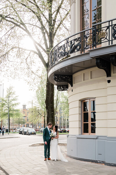 Een bruidspaar poseert voor een elegant, historisch gebouw tijdens hun bruiloft, vastgelegd door Monica Stout Fotografie in Rotterdam.