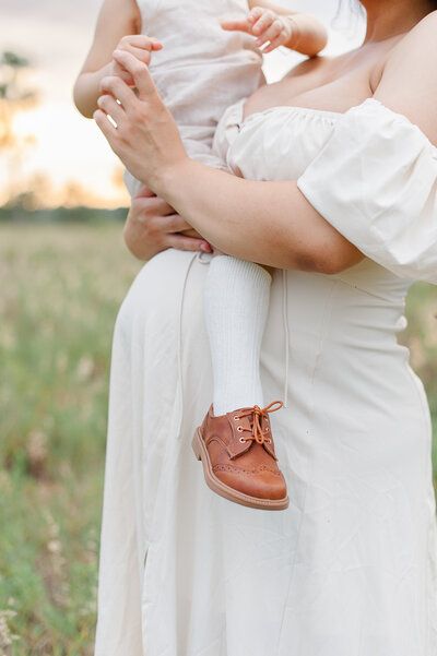 Close up of moms belly and toddlers feet during their family photo session in Cocoa Beach, Fl