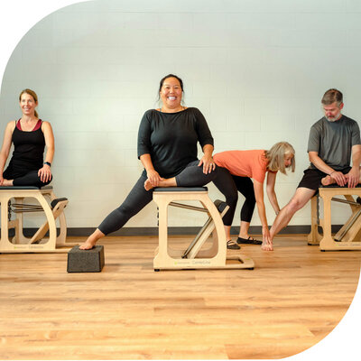 Group of three practicing mermaid on low chair at Pilates studio