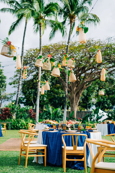 Luxury bespoke reception design at Fairmont Orchid Plantation Estates featuring rattan lanterns, blue textured linens, and wishbone chairs from Hawaii Island Events. Captured beautifully by photographer James Rubio