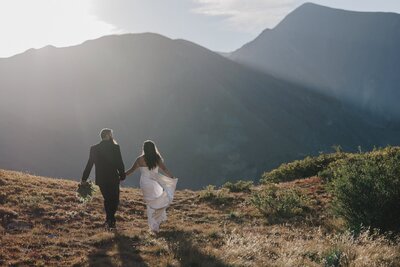 Bride and groom run toward mountain during Breckenridge golden hour.