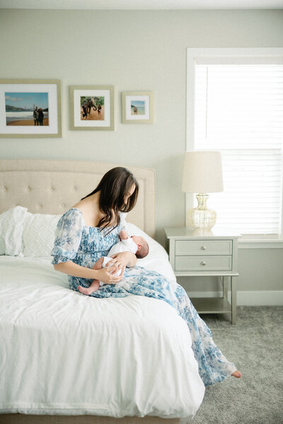 mom sitting on bed holding newborn baby during newborn photos