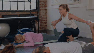 pilates instructor assisting two clients laying on mats in a class 