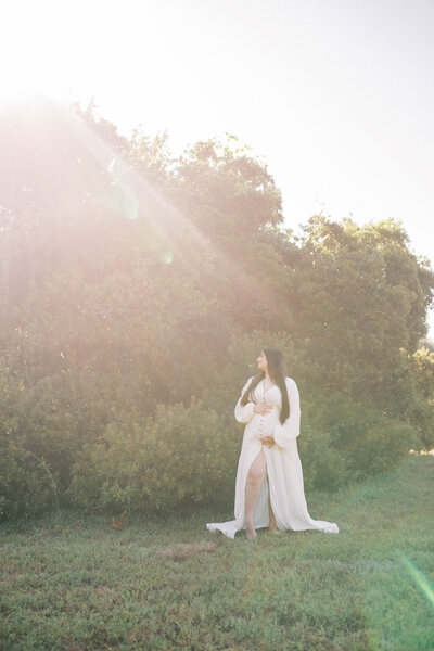 Maternity portrait taken at Camp Milton in Jacksonville as the sun rises over the trees and mom wearing a long white dress gazes into it