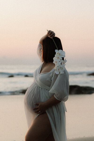 woman pregnant in flowy clothes walking on the beach watching the sunrise