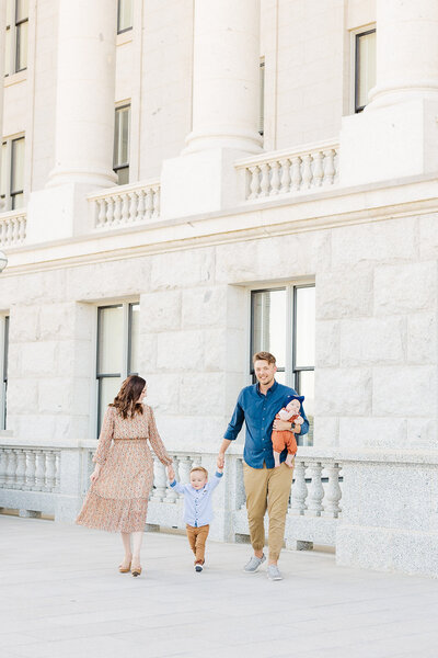 Family of 4 walking holding hands together during their family session at the Utah State Capital.