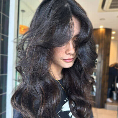 Brunette hair styled in voluminous waves with glossy highlights, captured in a modern hair studio.