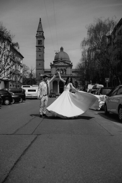 Ein glückliches Hochzeitspaar tanzt in einer Straße vor einer Kirche nahe dem Standesamt München.