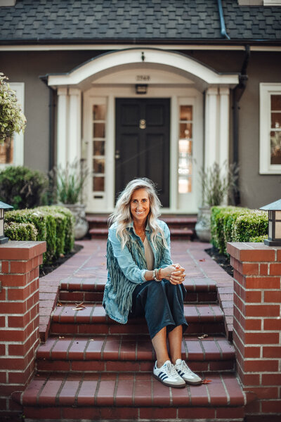Stephanie sits on a brick step walkway leading up to a house and smiles, representing how much she loves helping clients moving to Portland Oregon.