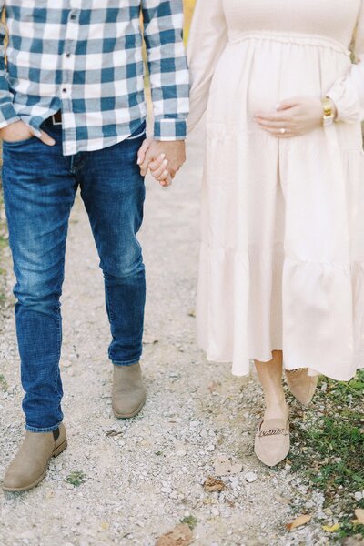 mom walking with hand on belly while holding husband's hand