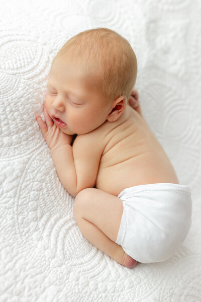 Newborn baby boy wearing white bloomers laying on an heirloom blanket in a studio in Savannah, Ga