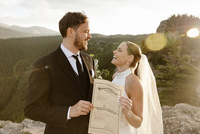 bride and groom holding marriage license on top of a mountain