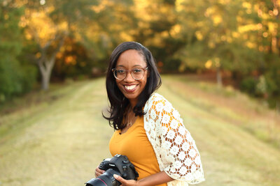Black South Carolina photographer holding her camera  in a park and smiling