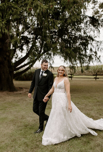 Bride and groom walking in field getting wedding portraits taken