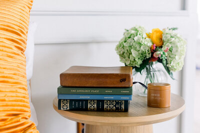 Stack of religious books on a table next to a candle and a vase of flowers