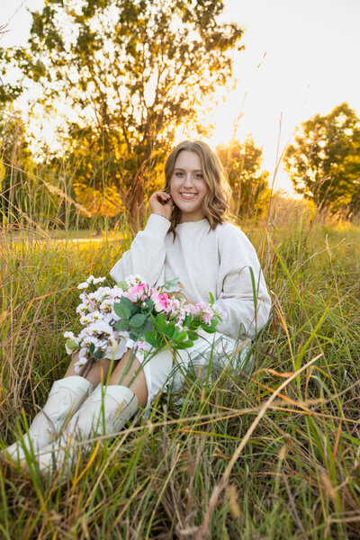 MBP Senior sitting in a grass field with flowers in her boots looking and smiling at the camera in Lawrence, KS