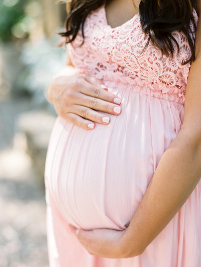 Expectant mother in a pink dress holds her belly during her maternity portrait session