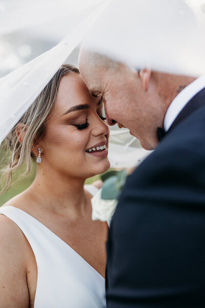 Bride and groom smiling at each other under veil. Taken at their Truffle Farm wedding in Canberra by wedding photographer, Acacia & Grace Photography