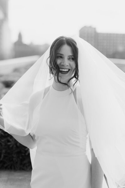 Black and white image of bride looking happy and over her shoulder with her veil