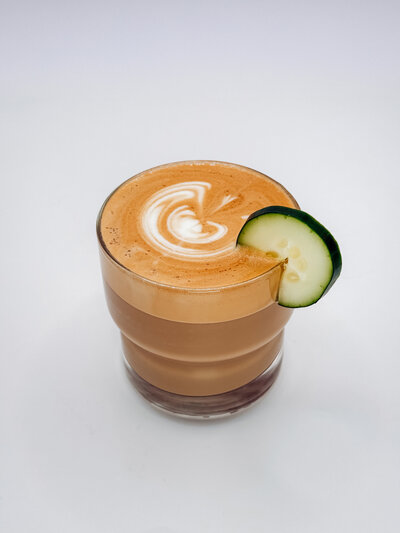 Glass of iced cucumber latte with latte art and fresh cucumber garnish – Quigley Coffee Co handcrafted specialty coffee.