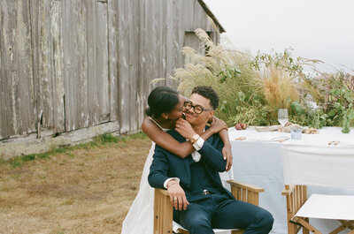 Bridal couple in suit and high neck wedding dress stand together at the alter with a green mossy backdrop during ceremony