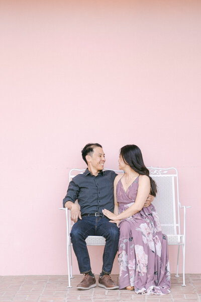 couple sitting on a bench in front of a pink wall