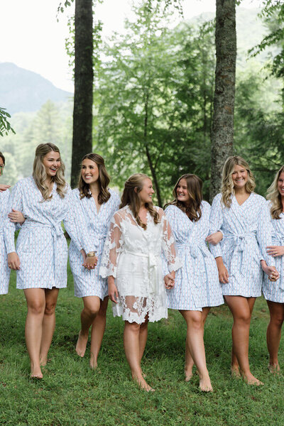 Bride and bridesmaids walk together linking arms in a field