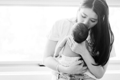 In-home newborn gallery in Sydney home with soft morning light with mother giving a forehead kiss to her newborn