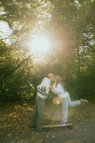 Couple in casual streetwear kisses over a longboard