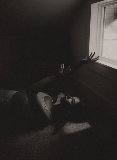 young girl laying on the ground under a window with her hands raised up towards to the light