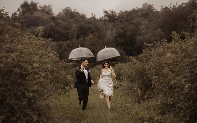 A couple running through a field with umbrellas in a whimsical wedding photo.