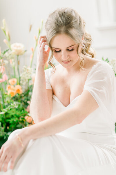 Close up of bride sitting in front of wildflowers, one hand on knees, one hand in her hair