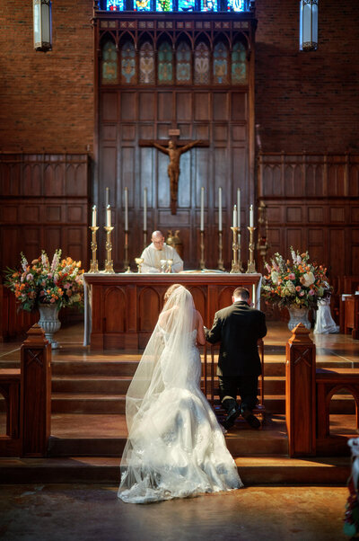 Bride and groom kneel at the altar during a catholic wedding ceremony