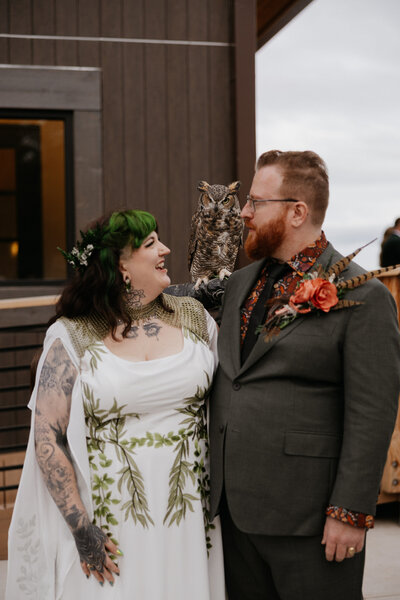 A newlywed couple smiling at an owl sitting on one of their arms 