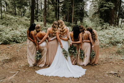 bride with her boho bridesmaids wearing champagne dresses in forest in Idaho holding bouquets, photo by Kaitlyn Neeley