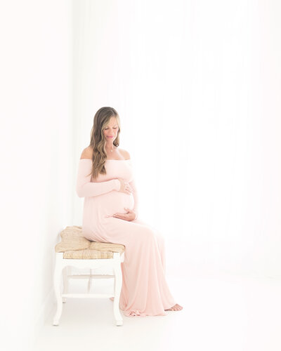 PregnPregnent womani n long pink dress cradling her baby bump