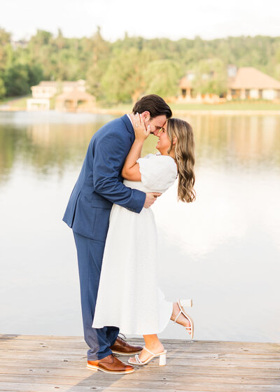 Julianna and Josh embracing on a dock with a serene lakeside backdrop, captured by Abby Bell Photography