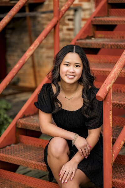Marvin Ridge High school grad posing in a black dress on a red staircase
