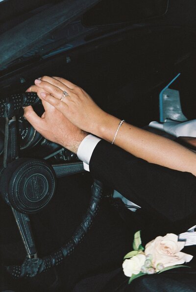 Bride and groom hold hands on steering wheel
