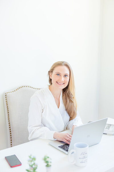 Washington DC Wedding Planner Kolena with Blue Sapphire Events sits at a desk with a laptop.